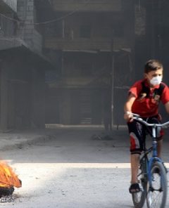 ALEPPO, SYRIA - AUGUST 4: Syrian children ride bikes as Syrian opponents burn tires to block the ground visibility of the war crafts belonging to the Russian Army and Assad regime forces at an opposition controlled neighborhood in Aleppo, Syria on August 4, 2016.  Ibrahim Ebu Leys / Anadolu Agency